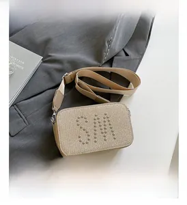 Close-up of beige crossbody bag with SM rivet logo and wide fabric shoulder strap