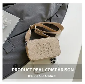 Detail of beige woven crossbody bag with silver SM rivet logo and wide strap next to phone