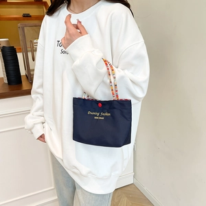 Navy blue canvas handbag with woven straps and gold lettering, lifestyle model shot