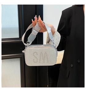Detail of silver glitter camera bag featuring metal rivet SM logo and wide fabric strap
