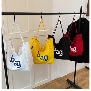 Detail view of large canvas tote bags in white, yellow, black, and red colors with bag print