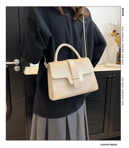 Detail of cream shoulder bag featuring faux croc texture and elegant gold metallic clasp