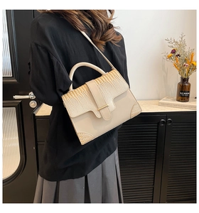 Détail de la couture en cuir à motif serpent sur sac beige avec barre dorée