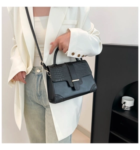 Detail of black crocodile-embossed leather handbag with metallic clasp on white blazer