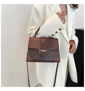 Detail of dark brown faux leather handbag featuring crocodile pattern and gold buckle