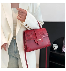 Detail of dark red handbag with crocodile texture accents and gold metal buckle