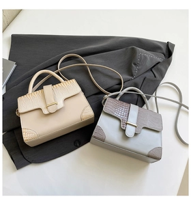 Détail de sacs beige et gris à motif crocodile sur un tissu gris foncé