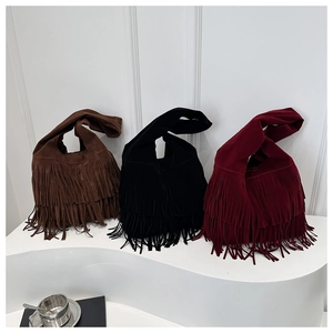 Three suede fringe tote bags in brown, black and burgundy on a minimalist white stand