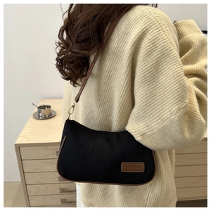 Detail of a minimalist black fabric shoulder bag with brown leather trim on a model