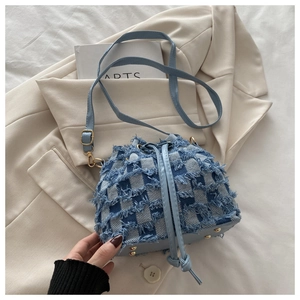 Close-up of checkered denim bucket bag with frayed tassel edges on a beige blazer