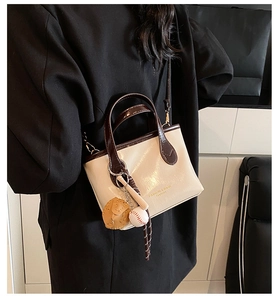 Detail of cream glossy leather bucket bag with contrasting dark brown handle and sports charm