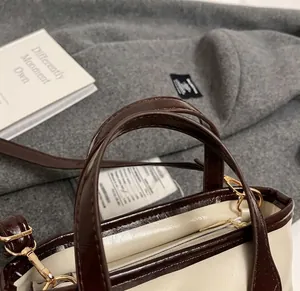 Close-up of cream leather tote handle with brown edges and gold-tone metal hardware