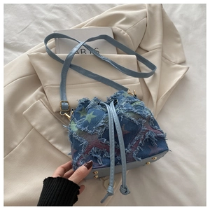 Detail of denim bucket bag showing colorful star patterns and frayed tassel edges