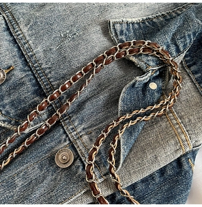 Détail de la chaîne argentée entrelacée de cuir marron sur fond en denim bleu