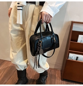 Detail of a black leather Boston bag with a tennis racket charm on a female model