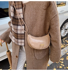 Photo de rue d'un sac demi-lune beige au fini brillant avec lettrage doré élégant