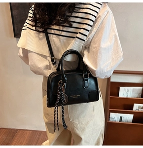 Detail of black leather handbag with gold lettering and striped rope charm accessory