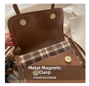 Close-up of vintage brown leather bag with dual magnetic snaps and plaid lining detail