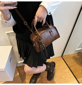 Close-up of a dark brown leather Boston bag with a tricolor braided cord and gold logo