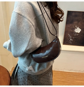 Détail d'un sac en demi-lune marron foncé en cuir brillant porté à l'épaule sur modèle