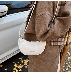 Gros plan d'un sac demi-lune blanc avec lettrage doré dans un décor de rue automnal