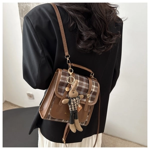 Detail view of brown plaid flap backpack with gold clasp and cute rabbit plush charm
