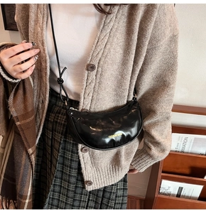 Sac à bandoulière noir en cuir brillant porté avec un gilet en maille de style rétro chic