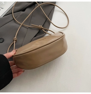 Gros plan du sac en croissant kaki avec logo doré et bandoulière fine à nœuds