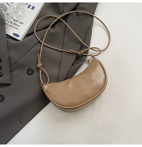 Détail du sac croissant beige avec bandoulière nouée sur un fond de costume gris
