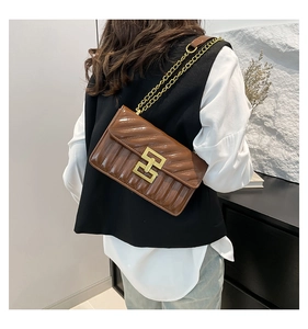 Braune gesteppte Ketten-Schultertasche mit Goldschließe an einem Model in Interieur