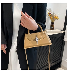 Detail of a beige mini handbag with silver star stud held by a model in home setting