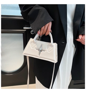 Nahaufnahme einer weißen Handtasche mit silbernem Sternanhänger und Gurt