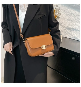 Gros plan d'un sac bandoulière en similicuir marron avec fermoir doré sur un blazer noir