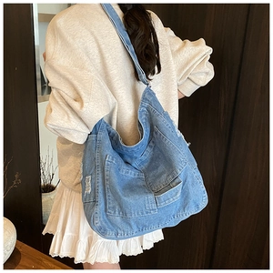 Detail of blue denim messenger bag featuring frayed edges and multiple front utility pockets