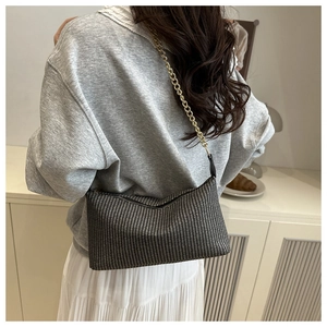 Detail of black and white woven pillow bag with a golden metal chain on a model