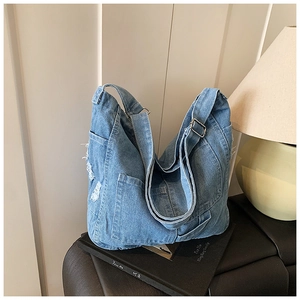 Detail of light blue denim tote bag with side pockets and vintage fringe on a decorative book
