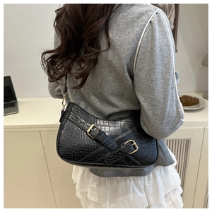 Detail of black faux crocodile leather shoulder bag with gold buckle on a model