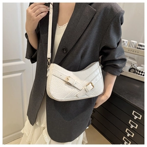 Detailed close-up of white crocodile pattern handbag with metal buckles on model