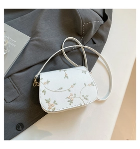 Détail de la broderie florale sur un sac selle blanc avec des crochets dorés