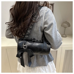 Detail of black cylindrical underarm bag featuring a large bow charm and metal ring