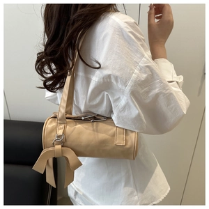 Detail view of a beige cylindrical shoulder bag with a stylish side bow and metal ring