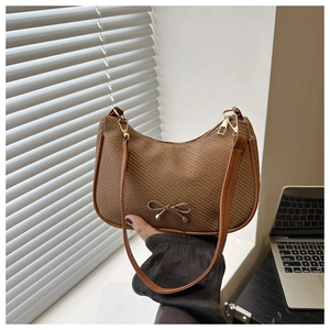 Detail of a brown woven crescent bag featuring a golden metal bow and shoulder strap