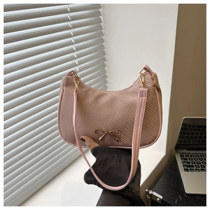 Close-up of pink woven handbag featuring a metallic gold bow clasp and shoulder strap detail