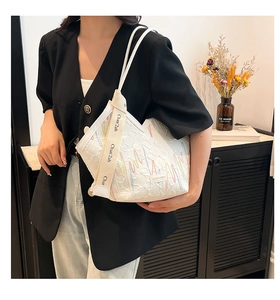 Detail of white canvas tote bag with wave embroidery and branded woven strap on a model
