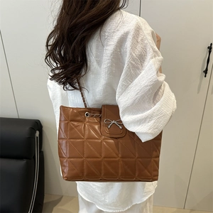 Brown quilted tote bag with silver bow accent worn by a model in a white shirt