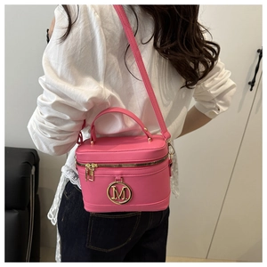 Detail of rose pink vanity case bag with gold M logo worn over a white shirt