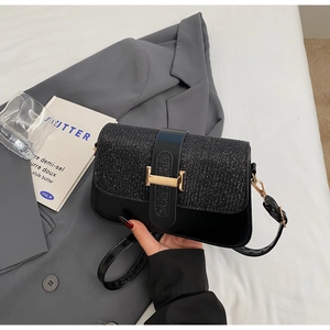 Close-up of elegant black square bag with shimmering texture and golden H-shaped buckle