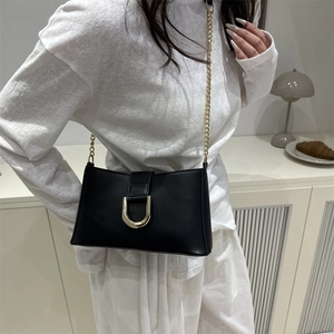 Minimalist black leather underarm bag with gold U-shaped buckle and chain strap shown on model