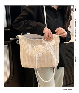 Close-up of white lace bow and leather brand label on woven straw bucket bag surface