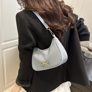 Light blue crescent shoulder bag with golden bow hardware on minimalist black blazer